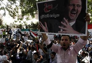 写真・図版 : カイロのシリア大使館前で、「人殺し閣下」と書かれたアサド大統領の写真を掲げて反政府デモに参加した人たち＝ＡＦＰ時事