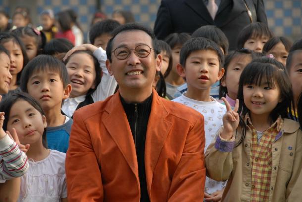 写真・図版 : 2006年に北京を訪れ、創立30周年を迎えた日本人学校で子供たちに囲まれたさだまさしさん