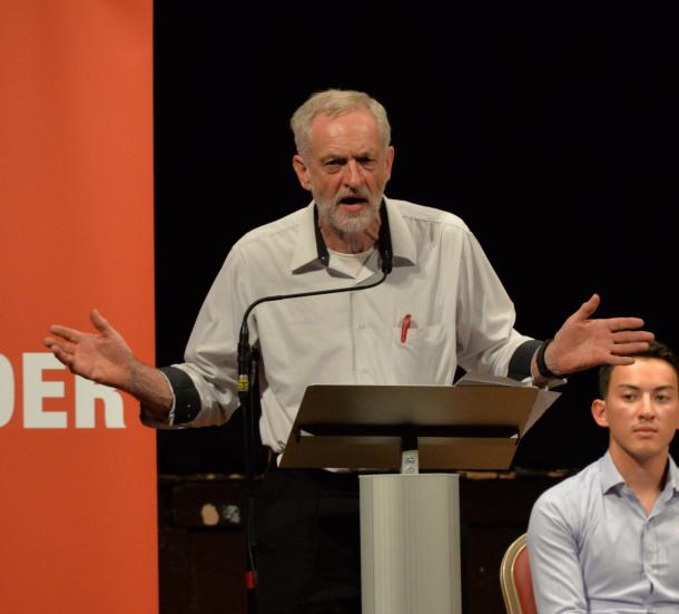 写真・図版 : ワイシャツの胸ポケットにペンをさしたラフないでたちで演説する英労働党の党首候補ジェレミー・コービン氏＝2015年8月
