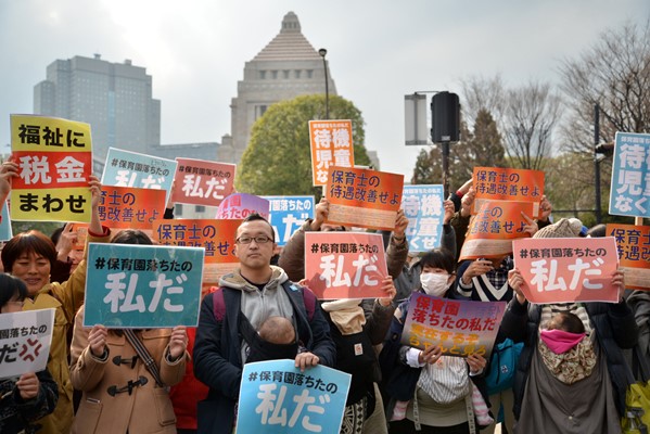 「保育園落ちたのは私だ」などと書かれた紙を掲げて立つ人たち＝2016年3月5日、東京都千代田区の国会議事堂前