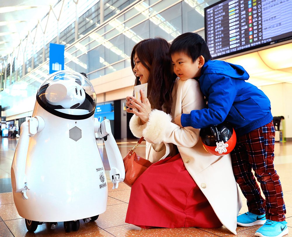 写真・図版 : 羽田空港内で親子と話をする案内ロボット「カイバ」＝2017年２月