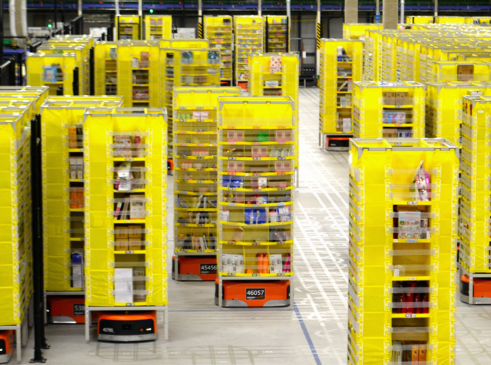 写真・図版 : 「商品棚」を運ぶ自走式ロボットが導入されたアマゾンの物流倉庫＝2016年12月、川崎市