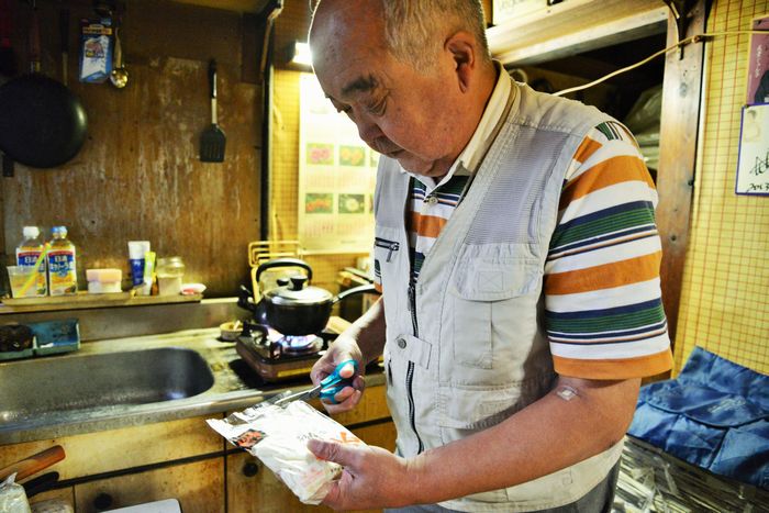 写真・図版 : 生活保護費切り下げの影響で、食費を削減。17円のきしめんの袋を切る男性＝名古屋市