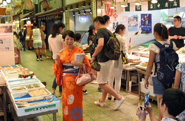 イカの串焼きを手に着物姿で記念撮影する外国人観光客＝2017年7月11日、京都市中京区の錦市場