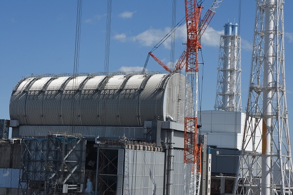 使用済み核燃料の取り出しを控えて、上部にかまぼこ形のカバーが設置された福島第一原発3号機の原子炉建屋。右奥には４号機上部の白いカバーも見える＝5月24日、松村北斗撮影