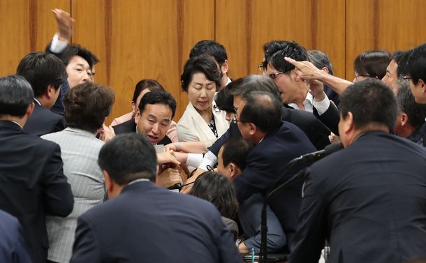 写真・図版 : 衆院内閣委でカジノ実施法案の採決が進められ、山際大志郎委員長（中央左）に詰め寄る野党委員ら。手前は起立する与党委員＝2018年6月15日