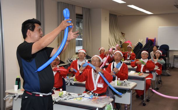 写真・図版 : 地域の社会福祉協議会が開いた「サンタクロース講座」で、講師に習ってバルーンアートを練習する定年退職した男性たち＝2017年11月、名古屋市中村区