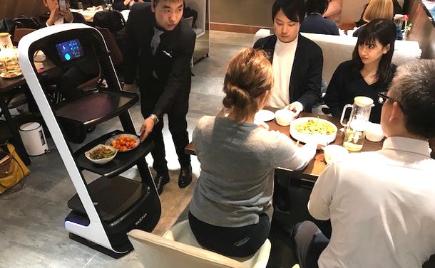 写真・図版 : 京東技術集団がオープンしたロボット・レストラン。ロボットが自動的に客のテーブルまで料理を運ぶ。まだ客も慣れていないので、まずは店員がロボットを手伝って配膳していた