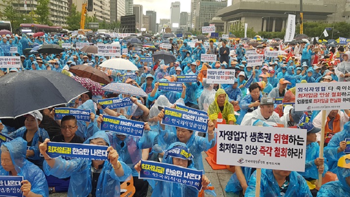 写真・図版 : ソウル中心部で2018年8月29日、豪雨のなかで開かれた最低賃金引き上げ政策に抗議する自営業者らの集会＝東亜日報提供
