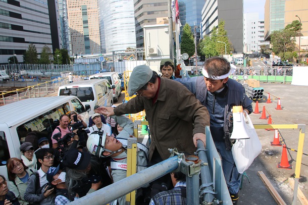 写真・図版 : ガードマンの妨害をはねのけて築地市場内(右側)に入ろうとする熊本一規さんと気遣う村木智義さん(マイクを持った人)=2018年10月18日、撮影・筆者