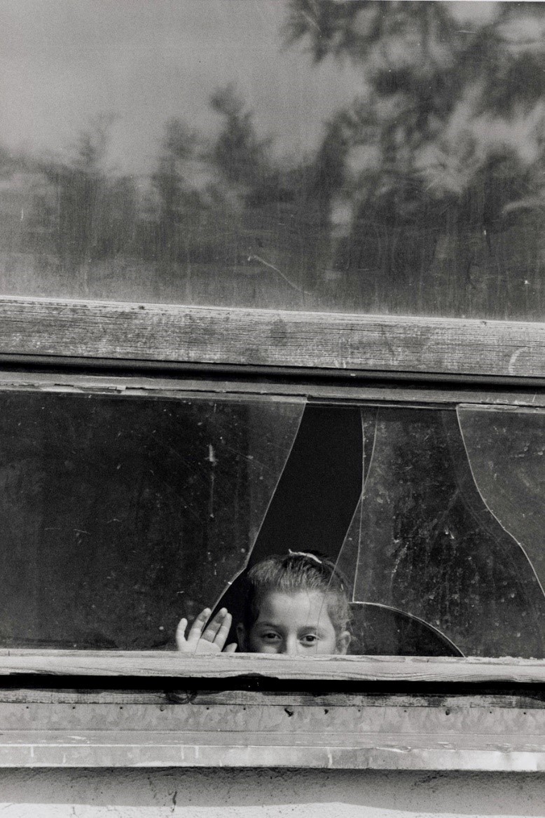 写真・図版 : 壊された校舎の修理はまだまだだ。窓からのぞく少女（コソボ、1999年）©Yoshino Oishi