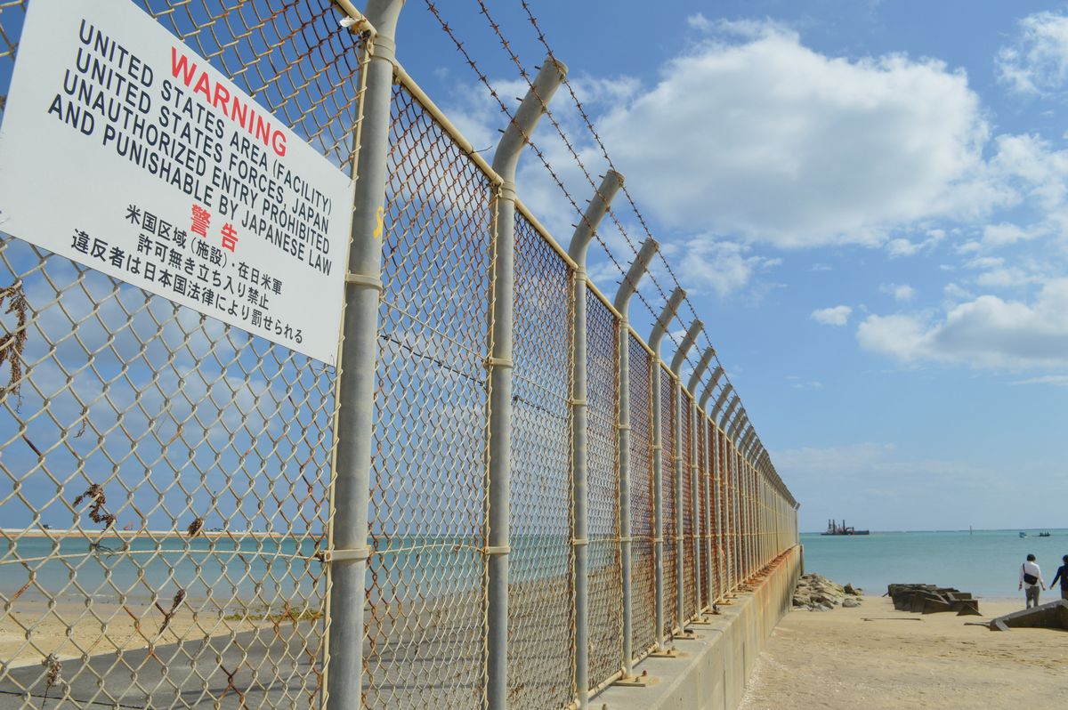 写真・図版 : 沖縄県名護市辺野古。フェンスの向こうの米軍基地の沖で、普天間飛行場を移設するための埋め立てが進む=2月下旬。藤田撮影