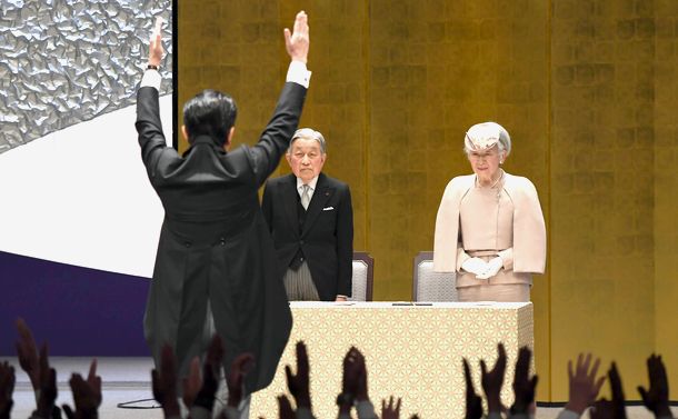 写真・図版 : 在位30年記念式典で、来場者の「万歳三唱」を受ける天皇、皇后両陛下（当時）。後ろ姿は安倍晋三首相＝2019年2月24日、東京・国立劇場