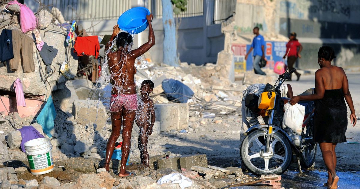 写真・図版 : ハイチ大地震で壊れた水道管から漏れる水で水浴びする人たち＝2010年2月7日、ハイチ・ポルトープランス