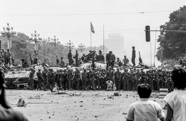 写真・図版 : 1989年6月4日、北京の天安門広場近くの長安街で1人の市民が捕まり、大勢の兵士の前でひざまずかされている。奥に見えるのは中国国旗 