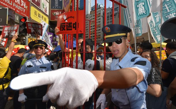 写真・図版 : 「逃亡犯条例」改正案に反対する民主派のデモ。中国本土の監獄に見立てたオリの中に入れられた民主派の男性を警察官役が監視するパフォーマンスもあった＝2019年4月28日、香港