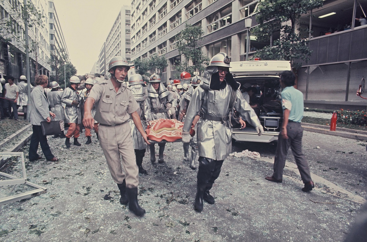 写真・図版 : 三菱重工ビル爆破事件。負傷者を搬送する消防職員と救急隊員＝1974年8月30日