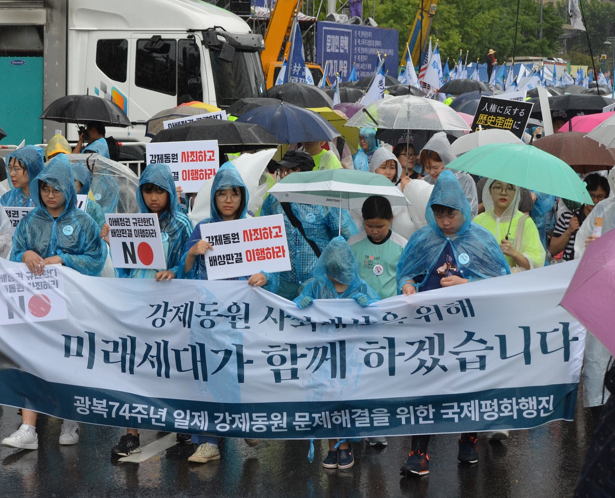 写真・図版 : 「強制動員を謝罪し　賠償判決を理解しろ」などと書かれたプラカードを持ち、ソウルの日本大使館に向かってデモ行進する元徴用工の支援者ら＝2019年8月15日