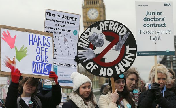写真・図版 : NHSの医師たちは2016年2月10日、ロンドンのセントトーマス病院の外で抗議。 給料と労働条件をめぐる論争で、数千人の若手医師が仕事を辞めた＝AP