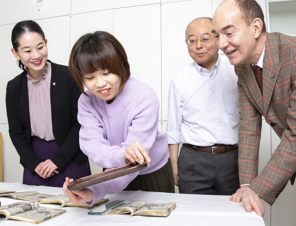 写真・図版 : 本を刷った版木を手に取る日本画家の松平莉奈さんと国文学研究資料館のロバート キャンベル所長（右端）。右から2人目は同館の入口敦志教授、左端は筆者
