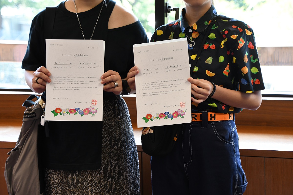 写真・図版 : 熊本市役所でパートナーシップの宣誓を終え、副市長から宣誓受領証をうけとった二人＝2019年8月8日
