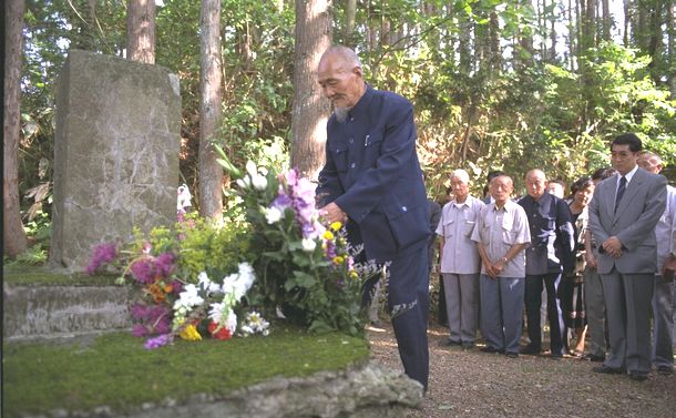 写真・図版 : 花岡事件から50年の1995年6月、現場近くに鹿島が建てた供養塔に献花する被害者代表・耿諄さん＝秋田県大館市