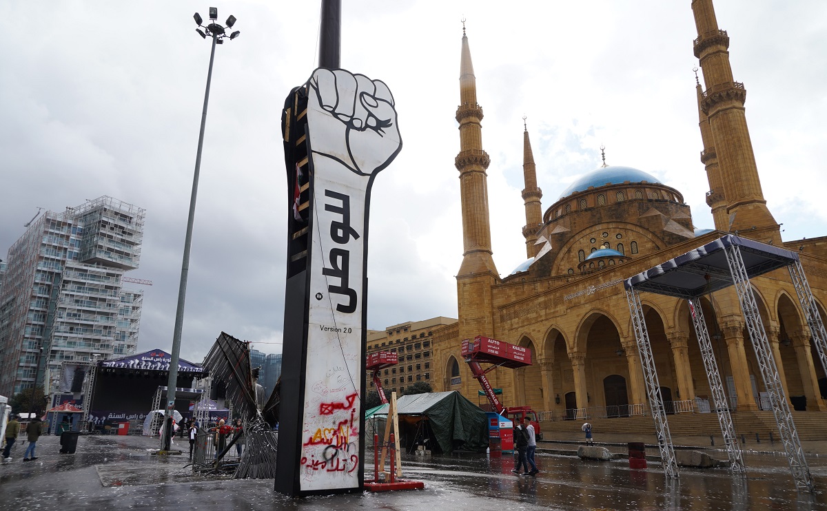 写真・図版 : ベイルートで反政府デモがおこなわれる広場には、抗議の象徴である拳を突き上げた形の看板が設置されていた=2020年1月1日