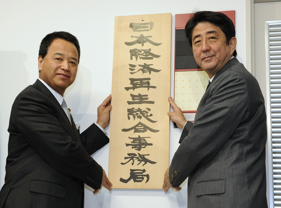 写真・図版 : 「日本経済再生総合事務局」の看板を掛ける安倍首相と甘利経済再生相＝2013年1月7日 、内閣府 
