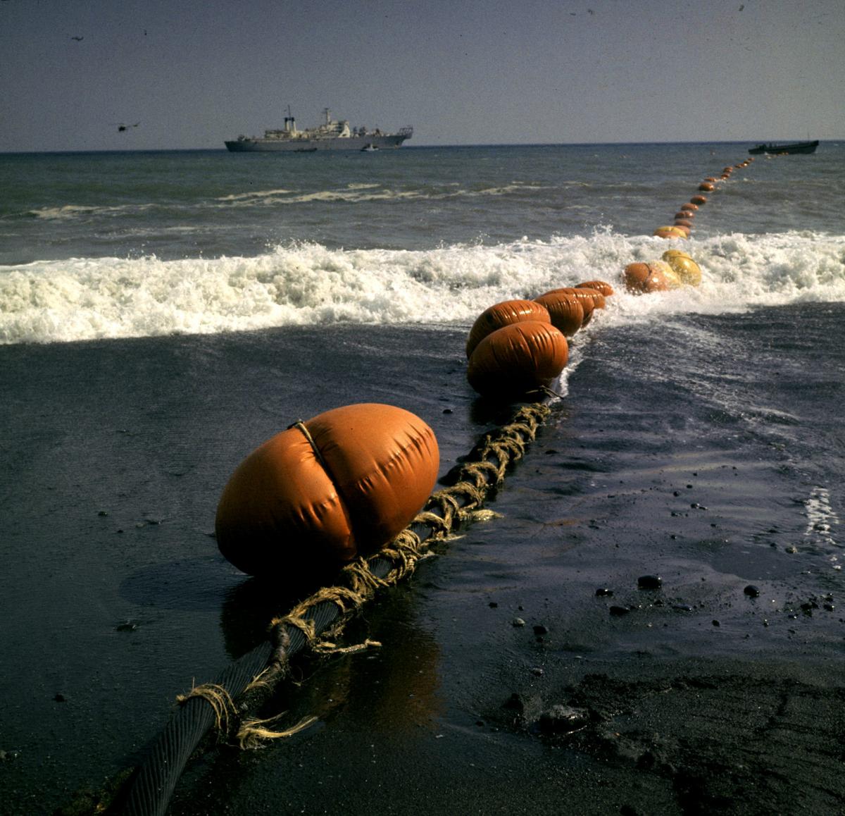 写真・図版 : 神奈川県の二宮海岸に陸揚げされた海底ケーブル。アメリカの海底ケーブル敷設船ロングラインズ号が1964年5月3日、神奈川県ニ宮町の海岸からグアム島に向けて、ケーブルを吐き出しながら15
日間の航海に出発した。ケーブルの先端が中継所に届いてから、赤い浮標は取り外され、ケーブルは海底に沈められた 