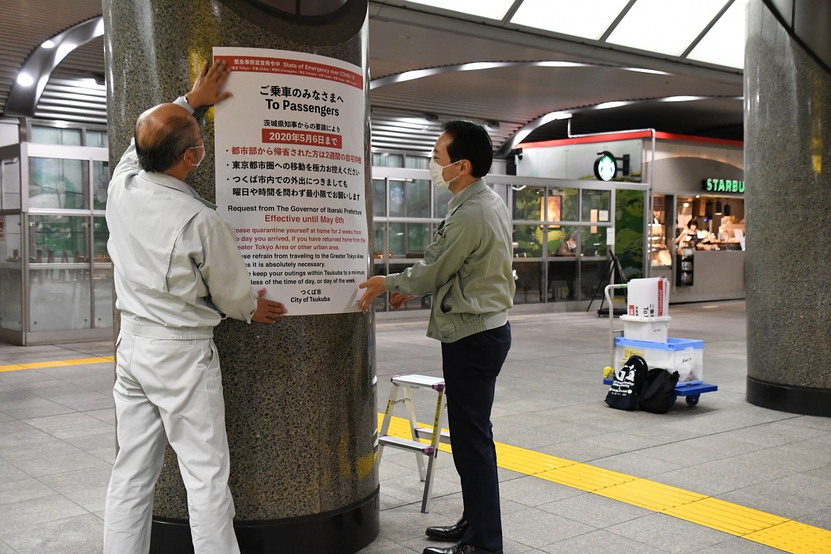 写真・図版 : 閑散とした駅の構内で外出自粛要請の貼り紙を貼る市の職員＝2020年4月9日、茨城県つくば市