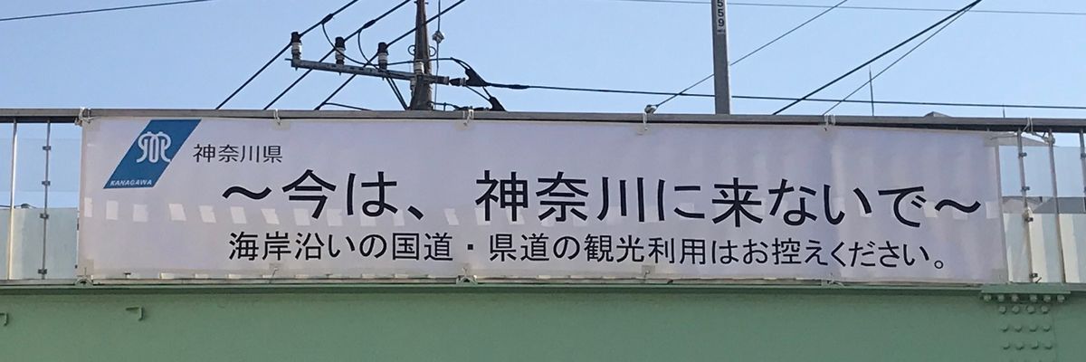 写真・図版 : 海岸沿いの国道や県道の観光利用を控えるよう「今は、神奈川に来ないで」と呼びかける神奈川県の横断幕が、湘南地方へ向かう国道にかかる