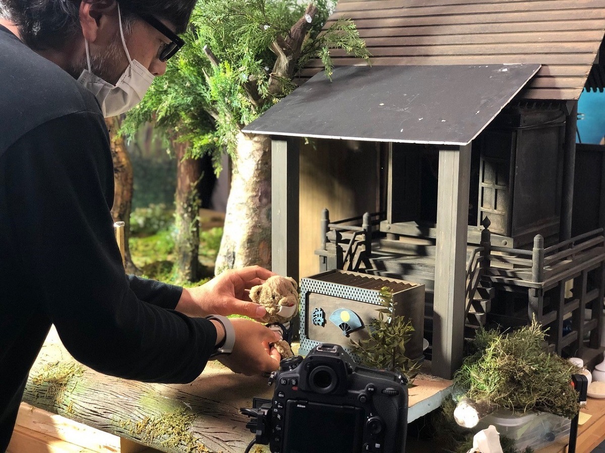 写真・図版 : 『春になったら こぐまのユーゴ物語』を撮影中の村田朋泰監督。監督と同じように、こぐまのパペット(人形)もマスクを着用している　(C)TMC