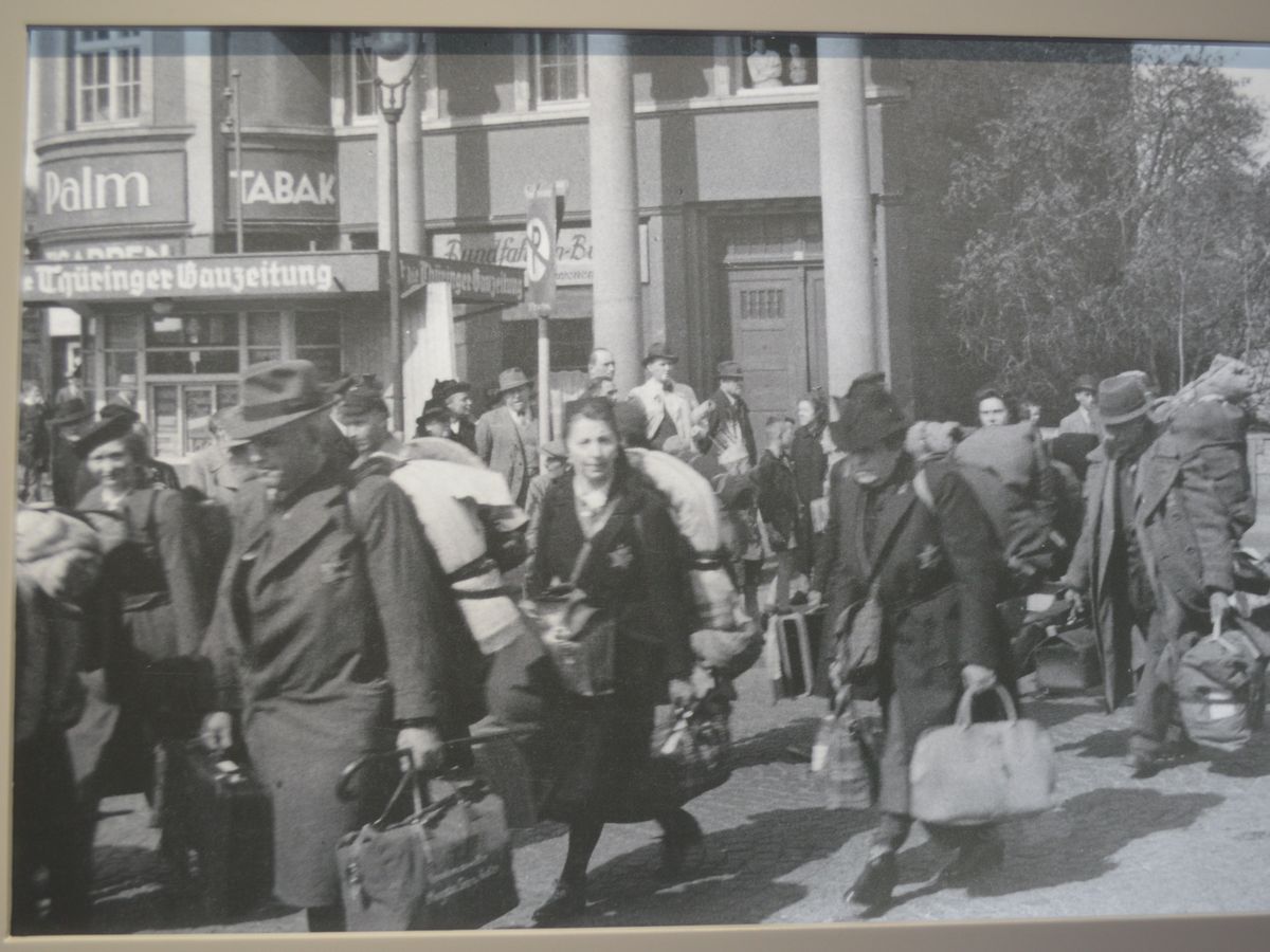写真・図版 : ナチスによる強制移送で街中を歩くユダヤ人たちと、それを見るドイツの人々=ヴァンゼー会議の史料館の展示より