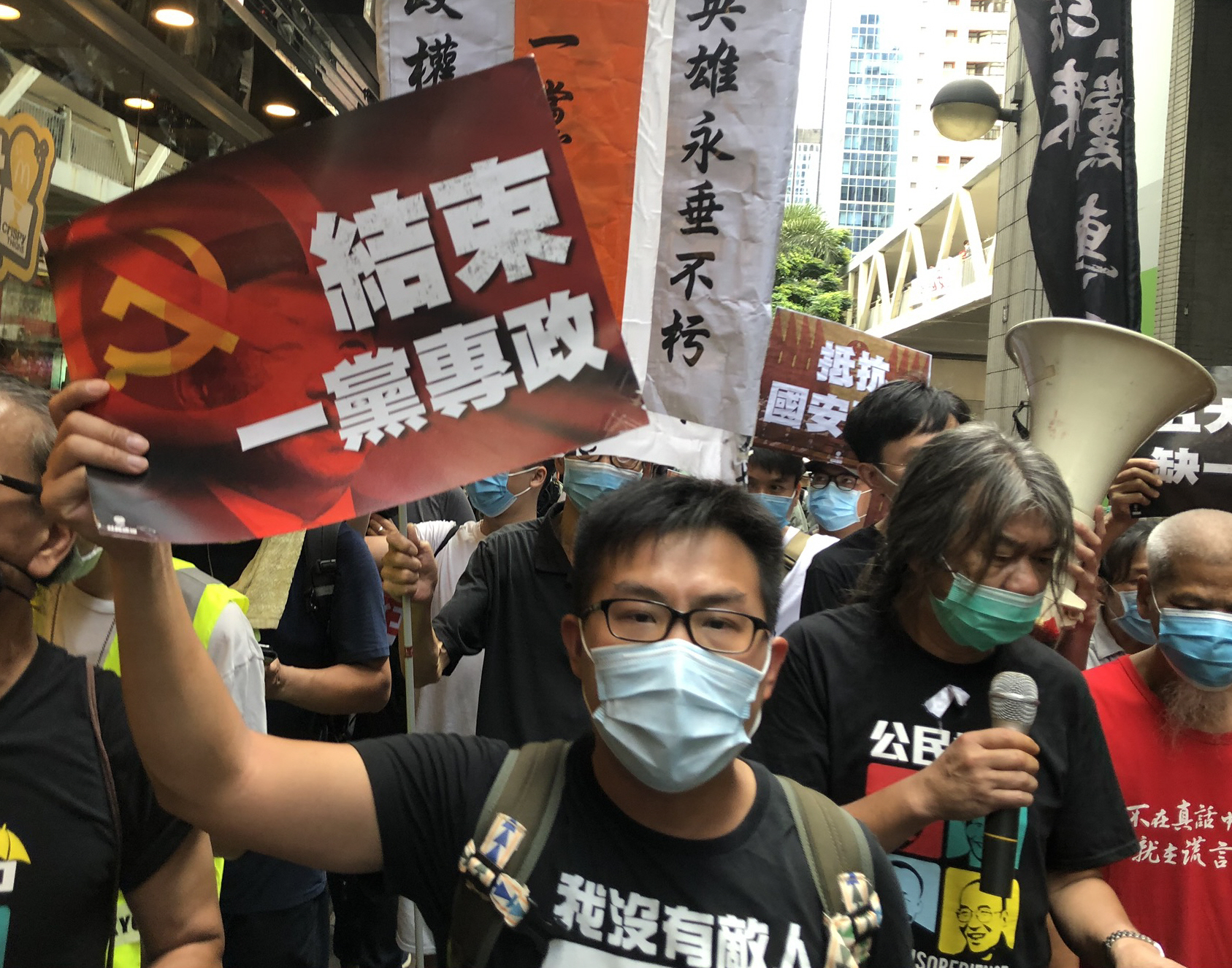 写真・図版 : 香港国家安全維持法の施行に反対するデモ行進で、「（中国共産党の）一党独裁を終わらせよ」と書かれたビラを掲げる参加者（中央）ら＝2020年7月1日、香港