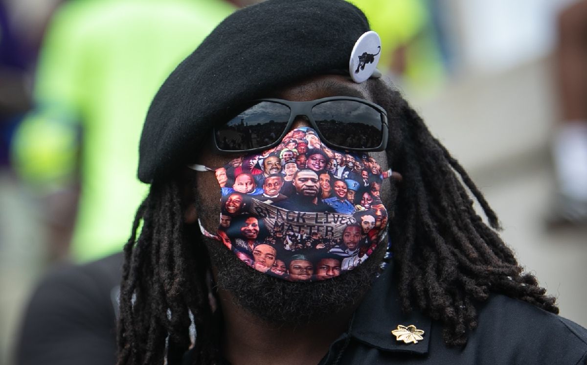 写真・図版 : 犠牲者の顔がデザインされたマスクをして、人種差別に抗議するイベントに参加する男性＝2020年8月28日、ワシントン、ランハム裕子撮影
