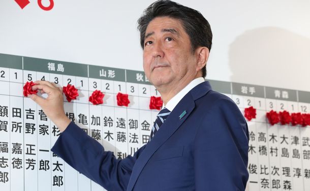 写真・図版 : 自公の与党が大勝。当選を決めた候補者名に花をつける自民党の安倍晋三総裁＝2017年10月22日、東京・永田町 

