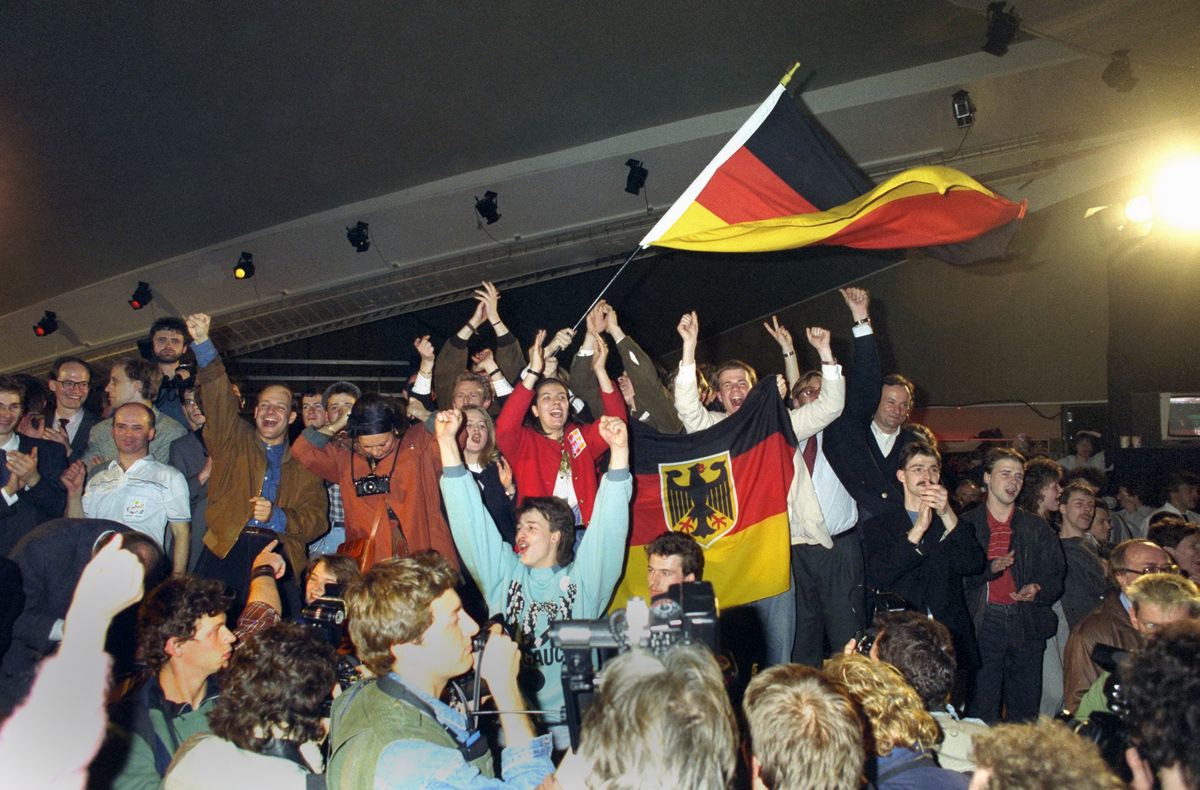 写真・図版 : 1990年3月、東ドイツの総選挙で西ドイツとの早期統一を求める勢力が勝ち、東ベルリンで西ドイツの国旗を振って喜ぶ人々=朝日新聞社