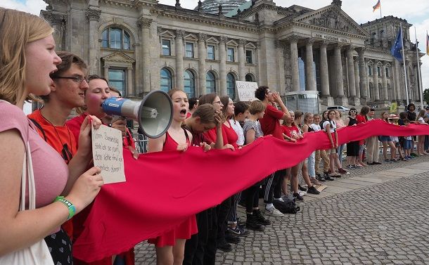 ドイツ連邦議会の建物を赤い布を持って取り囲み、地球温暖化対策を訴える人たち＝2019年6月28日、ベルリン、野島淳撮影  