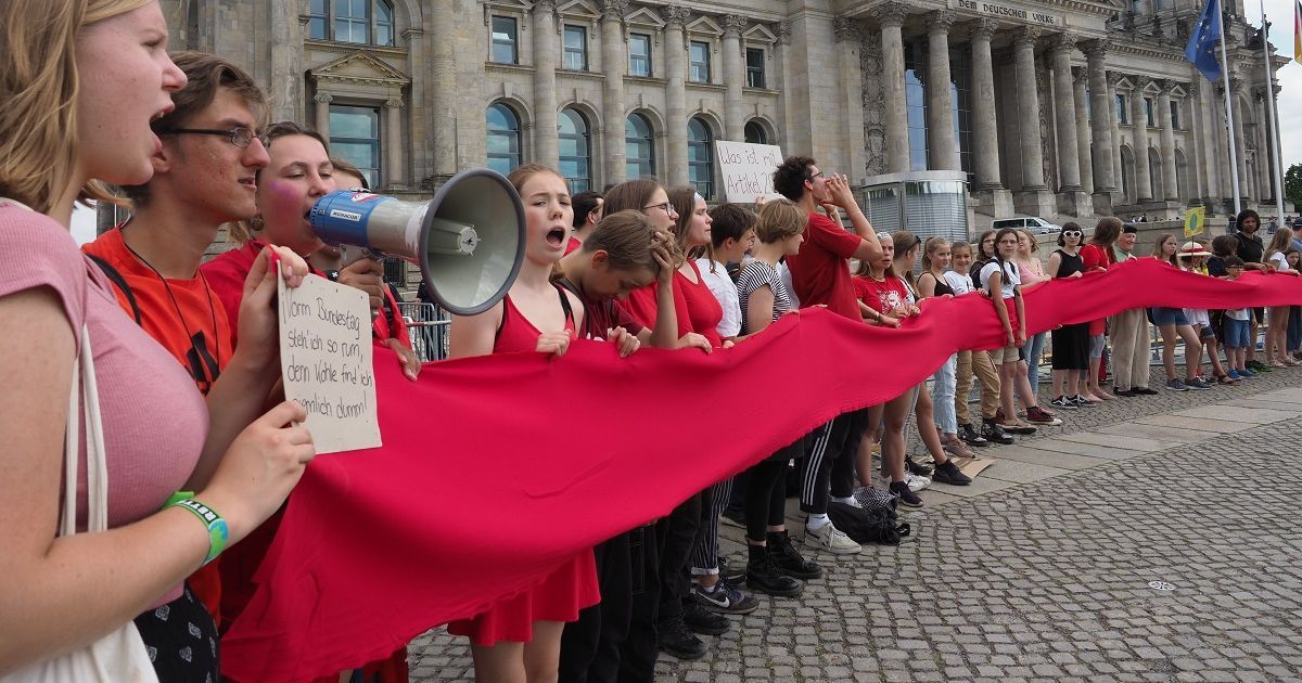 写真・図版 : ドイツ連邦議会の建物を赤い布を持って取り囲み、地球温暖化対策を訴える人たち＝2019年6月28日、ベルリン、野島淳撮影  