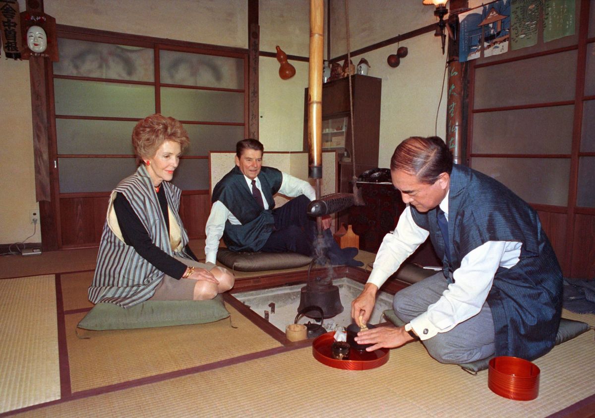 「日の出山荘」の囲炉裏を囲んで中曽根康弘首相が茶を点てる様子を見つめるアメリカのレーガン大統領とナンシー夫人=1983年11月11日、東京都日の出町、代表撮影