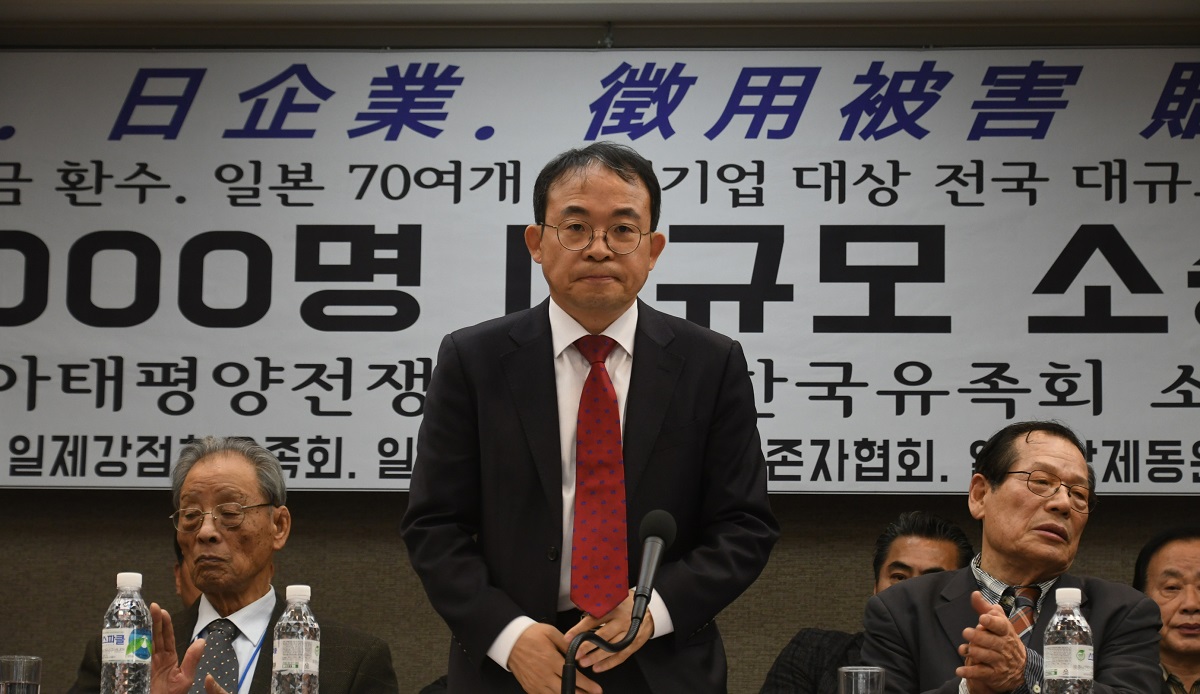 写真・図版 : 韓国政府に対してソウル中央地裁に提訴した後、記者会見する弁護士(中央)と原告団の元徴用工 =2018年12月20日