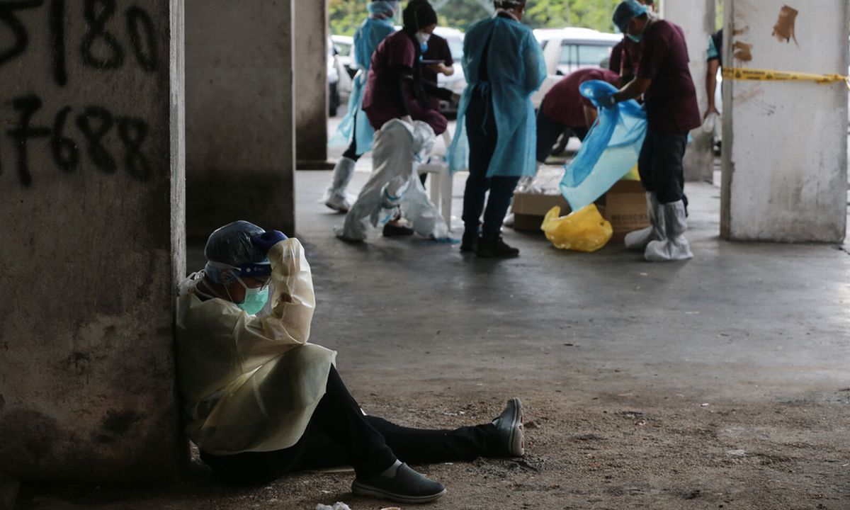 写真・図版 : 1日中途切れない新型コロナウイルスの検査を担い、わずかな休憩時間に座り込む医療従事者＝10月21日、マレーシア・クアラルンプール（Yuri Abas/Shutterstock.com）
