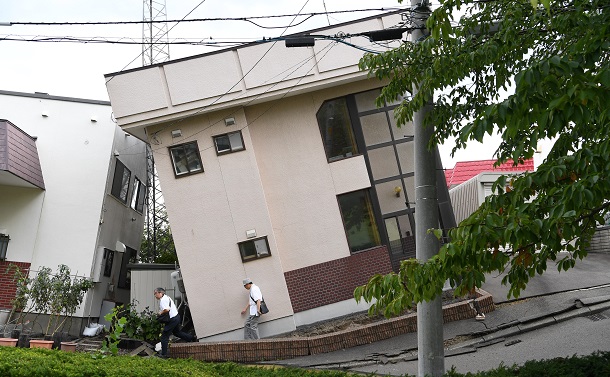 写真・図版 : 震度6強の地震で道路が陥没し、傾いた住宅＝2018年9月6日、札幌市