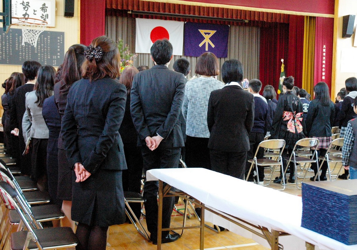 写真・図版 : 卒業式で君が代を起立斉唱する大阪市立小学校の教職員。大阪市では2011年、「自治体教職員は学校行事で行う国歌斉唱は起立により斉唱する」とした〝君が代条例〟が制定された＝2012年3月21日