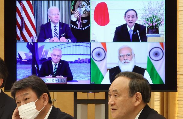 写真・図版 : オンラインで会談する日米豪印の首脳。手前右は菅義偉首相。画面内は（右下から時計回りに）モディ印首相、モリソン豪首相、バイデン米大統領＝2021年3月12日、首相官邸 