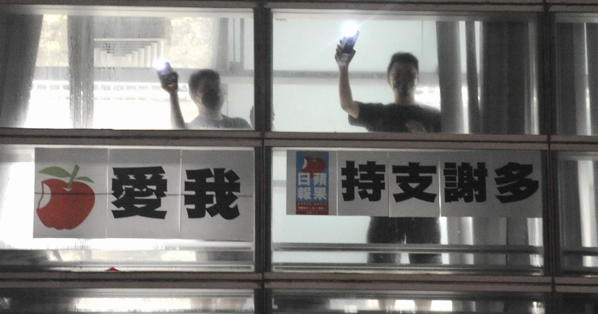 写真・図版 : 「リンゴ日報」の編集局から、本社前に集まった市民にスマホの光を照らして感謝の気持ちを伝える社員。「支持をありがとう」とのメッセージも掲げられた＝2021年6月23日、香港