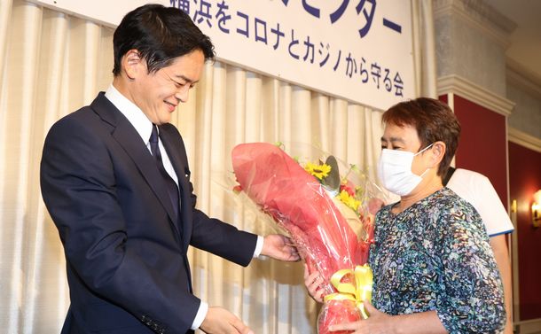 写真・図版 : 横浜市長選で当選を決め、支援者から花束を贈られる山中竹春氏（左）＝2021年8月22日、横浜市中区