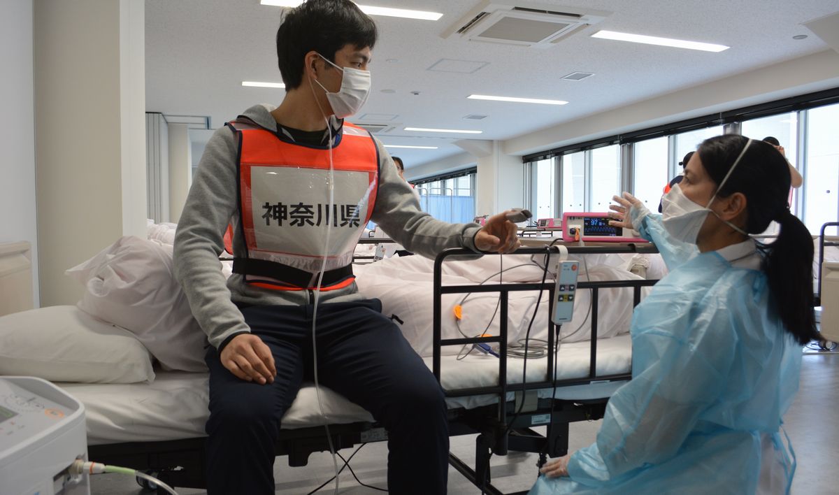 写真・図版 : 神奈川県は2月、準備が整った緊急酸素投与センター（酸素ステーション）を報道陣に公開し、療養の様子を実演した。この時は当面、稼働させない方針で、知事は「使われないことがベストシナリオ」と語っていた＝2021年2月2日、神奈川県立スポーツセンター