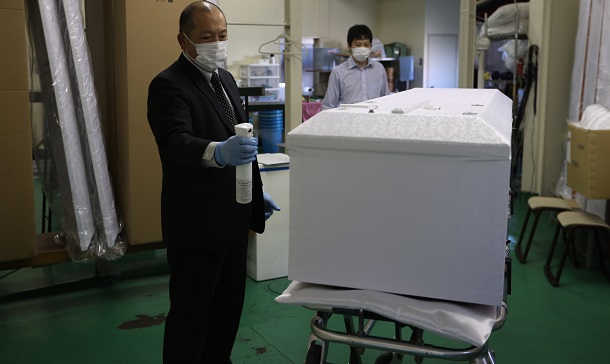 写真・図版 : 新型コロナウイルスの感染が疑われる遺体の入った棺を冷蔵安置室から出し、消毒する葬儀会社の従業員＝2020年5月、東京都板橋区