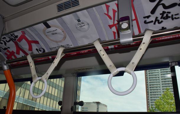 写真・図版 : バスのつり革と体操のつり革の大きさを比較する西日本工業大学の学生が制作した車内ポスター＝2021年9月16日、北九州市